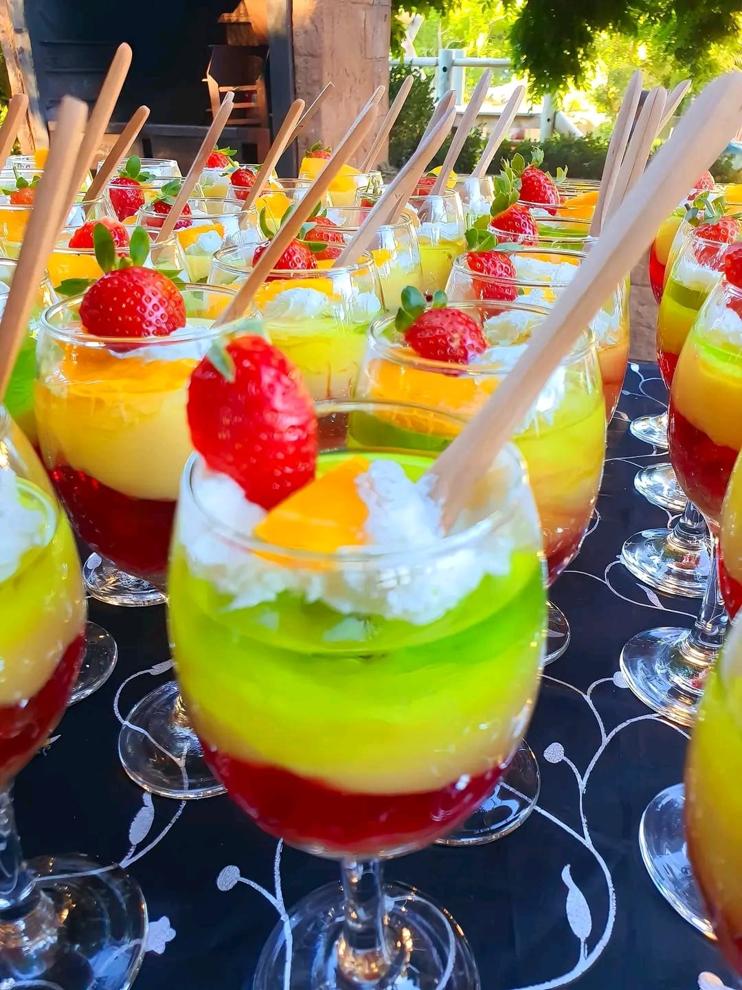 Rows of rainbow layered dessert cups with fresh strawberries at outdoor event